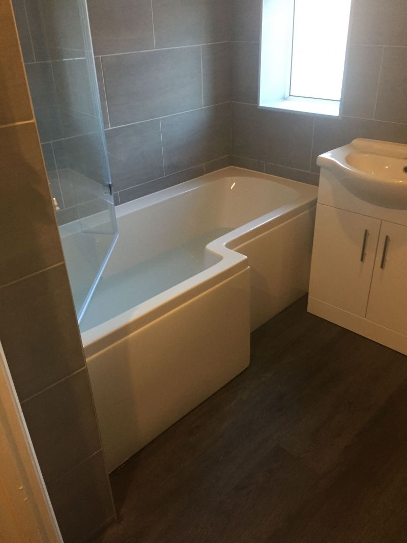 Bath & Shower Room, L Shaped Bath with double headed shower, glass shower screen, vanity unit, close couple toilet.  Inara concrete tiles, Dark Grey vinyl click flooring & chrome raditor towel rail.: Swipe To View More Images