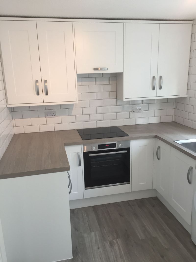 Howdens Chelford White kitchen range, Brushed steel effect Bow D Handles together with Grey Oak Effect Square Edged worktops complimented with a Light Grey Oak Vinyl Flooring. 

Appliances Bosch, Integrated Extractor, Frankie Ascona sink and Swan neck tap.   White brick effect tiling.: Swipe To View More Images