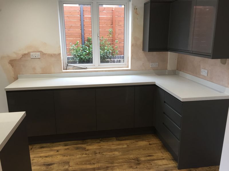 Howdens Clerkenwell Kitchen Super Matt integrated handle door in Graphite with Storm Grey Quartzstone worktops and upstands with a contrasting Vinyl Click flooring in Chestnut.: Swipe To View More Images