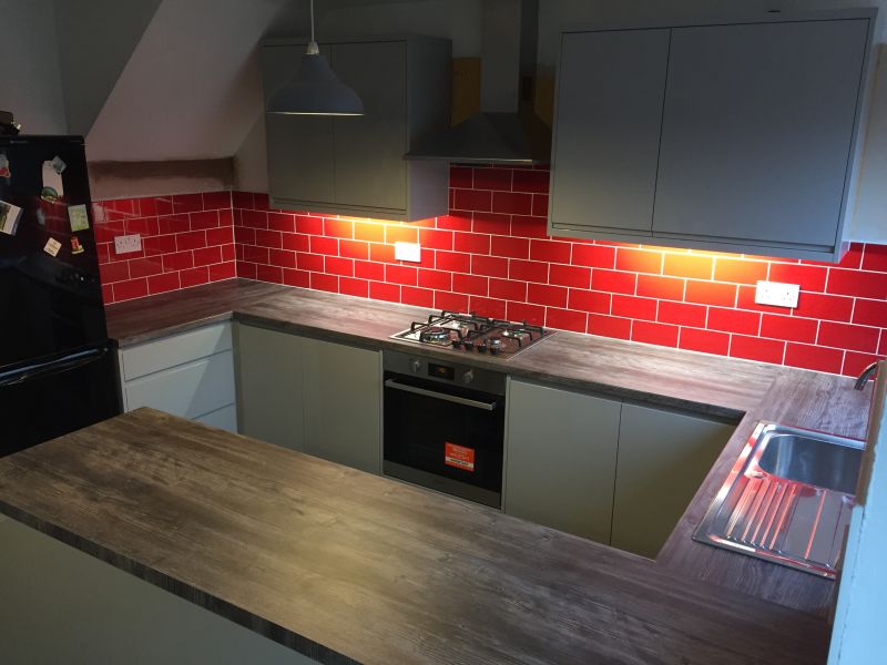 Homebase Handleless Gloss Grey Kitchen Range, Pine Grain worktops and stainless steel appliances.  Red brick effect tiling.: Swipe To View More Images