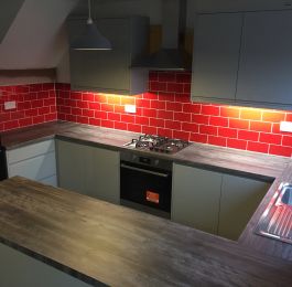 Homebase Handleless Gloss Grey Kitchen Range, Pine Grain worktops and stainless steel appliances.  Red brick effect tiling.: Click Here To View Larger Image